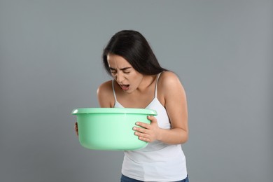 Young woman with basin suffering from nausea on grey background. Food poisoning