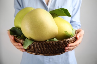 Photo of Woman holding basket with fresh pomelo fruits on light background, closeup