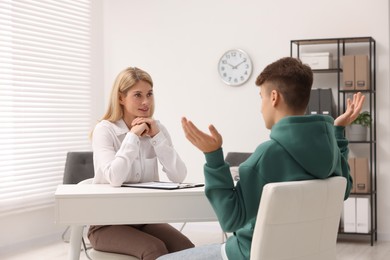 Psychologist working with teenage boy at table in office