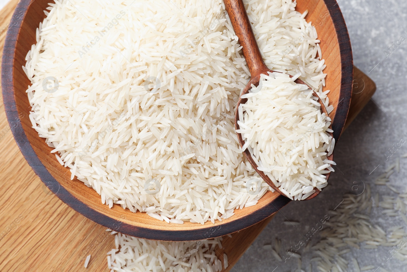 Photo of Raw basmati rice in bowl and spoon on grey table, top view