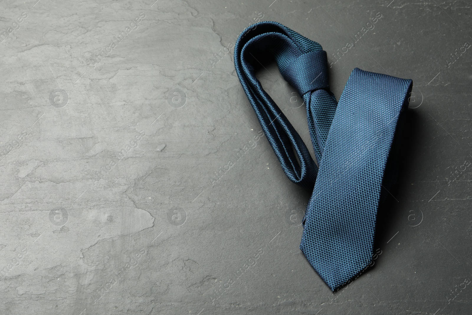 Photo of One blue necktie on grey textured table, top view. Space for text