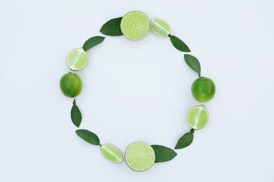 Photo of Frame made of fresh ripe limes and green leaves on white background, flat lay. Space for text