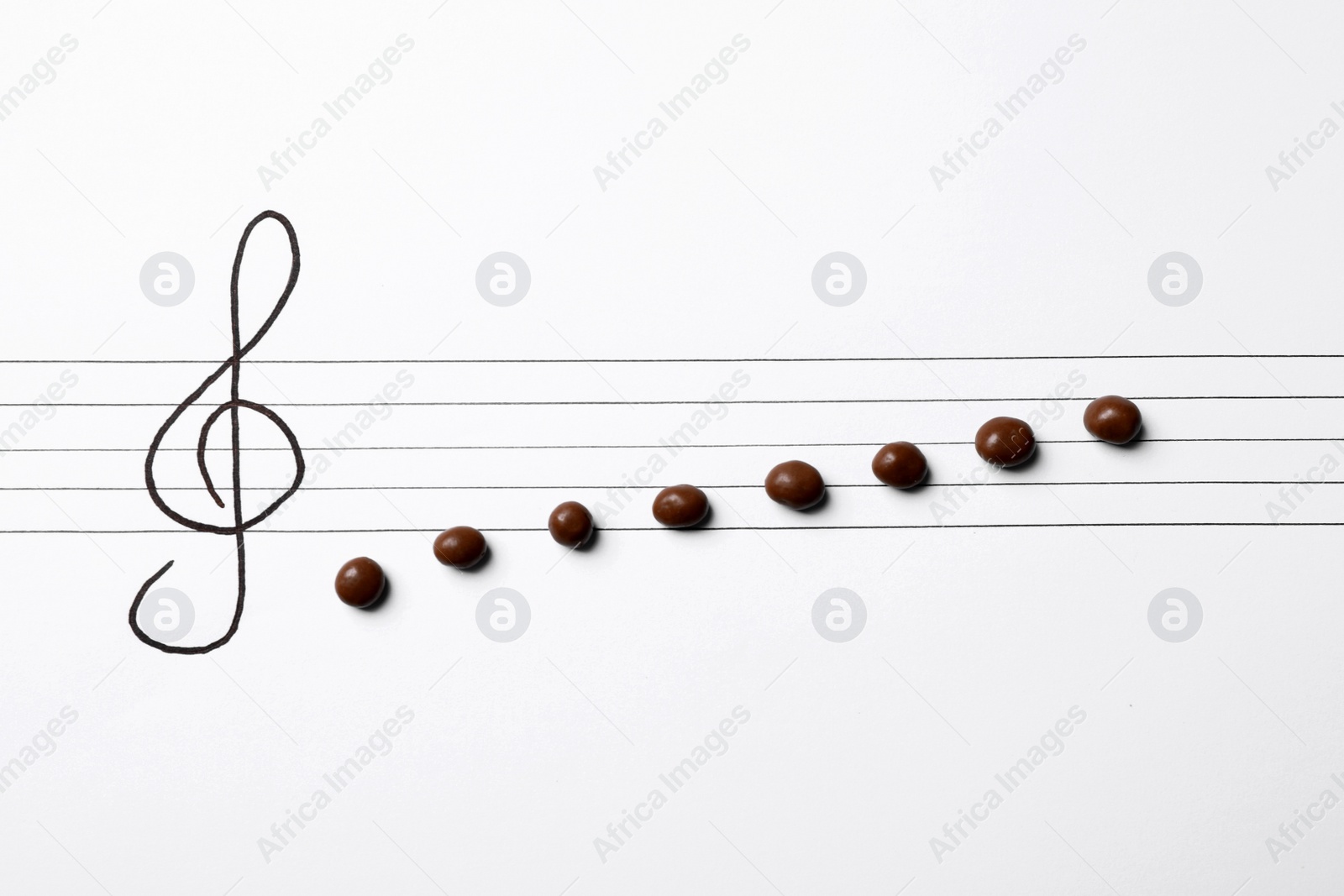 Photo of Music staff with treble clef and chocolate candies as notes on white paper, flat lay. Creativity concept