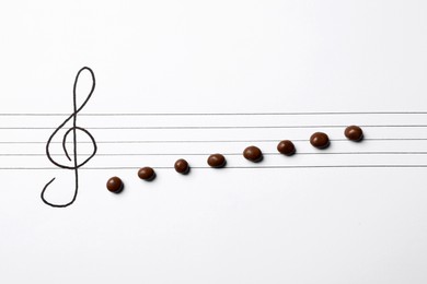 Photo of Music staff with treble clef and chocolate candies as notes on white paper, flat lay. Creativity concept