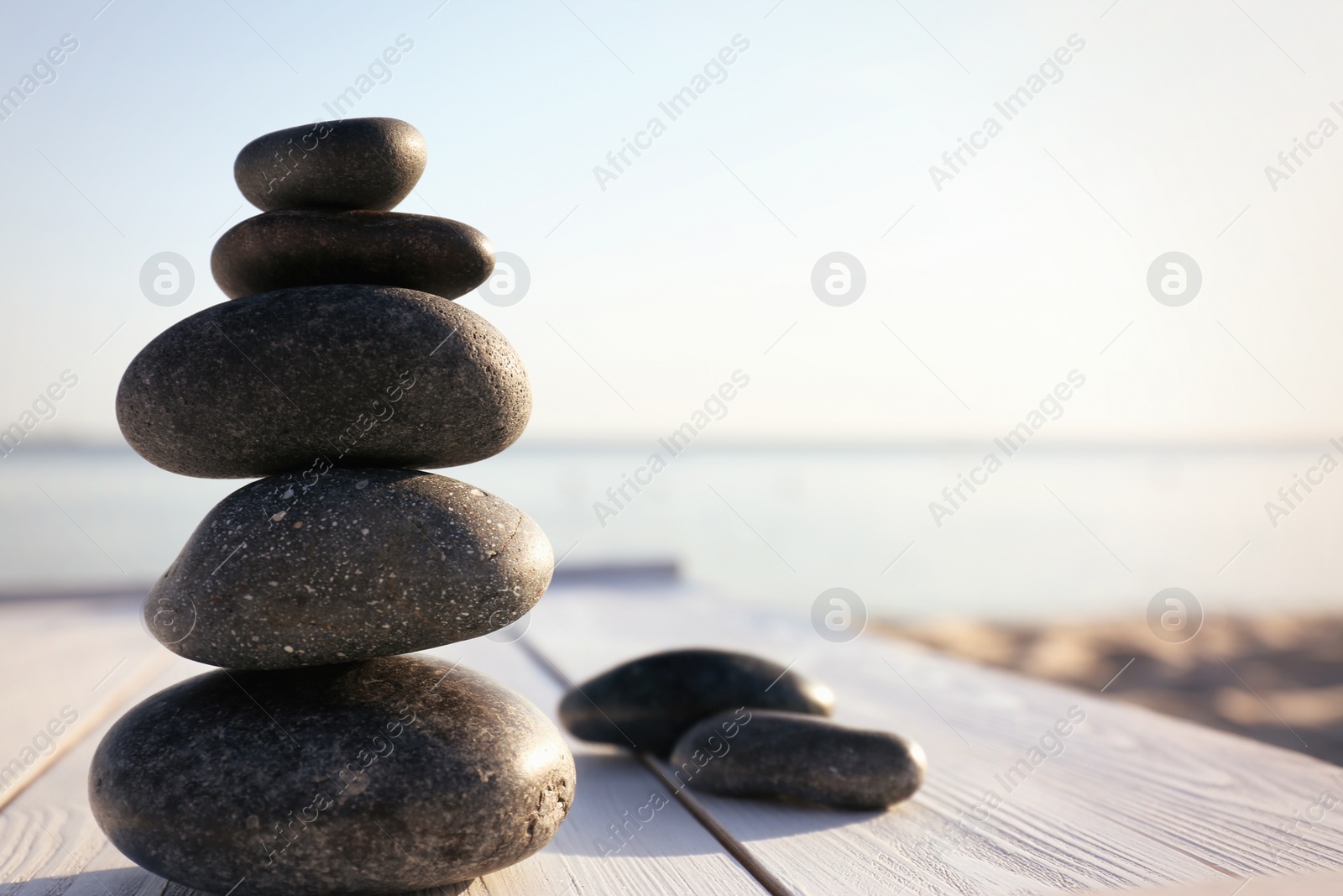 Photo of Stack of dark stones on wooden deck near sea. Zen concept