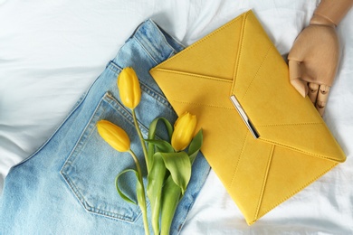 Photo of Composition with stylish envelope bag and flowers on crumpled white sheet, flat lay