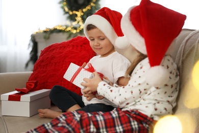 Cute children holding gift box on sofa in room decorated for Christmas