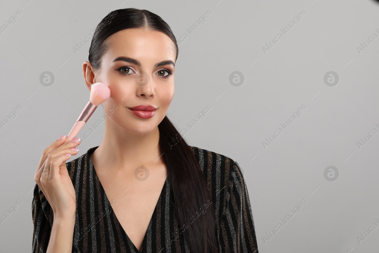 Photo of Everyday makeup. Beautiful woman applying face powder on light grey background, space for text