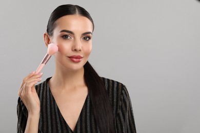Everyday makeup. Beautiful woman applying face powder on light grey background, space for text