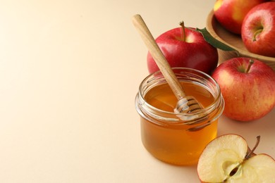 Photo of Delicious apples, jar of honey and dipper on beige background. Space for text