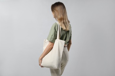 Woman with blank eco friendly bag on light background, back view