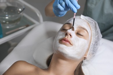 Photo of Cosmetologist applying mask on client's face in spa salon