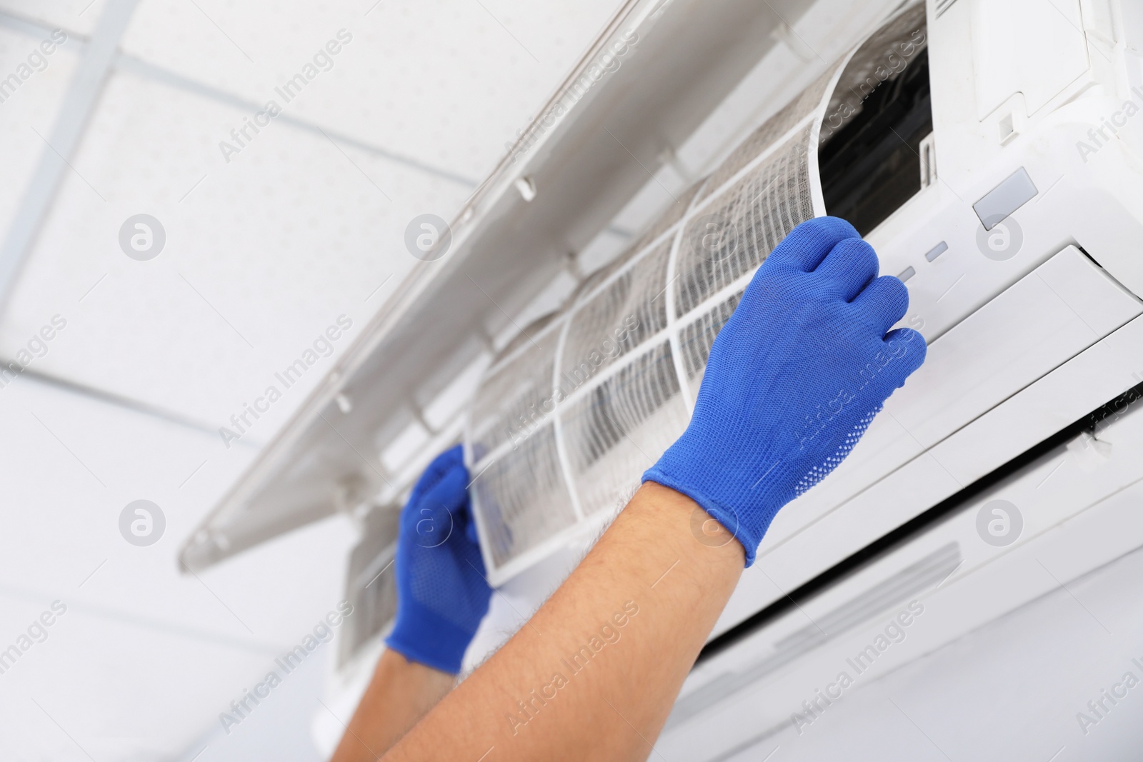 Photo of Professional technician maintaining modern air conditioner indoors, closeup