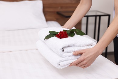 Photo of Chambermaid putting fresh towels with flower on bed in hotel room, closeup