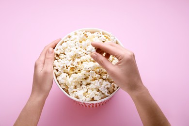 Woman taking fresh popcorn from bucket on pink background, above view