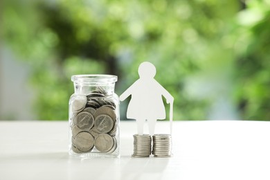 Photo of Pension savings. Figure of senior woman and jar with coins on white table against blurred green background