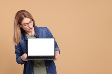 Emotional woman showing laptop on beige background. Space for text