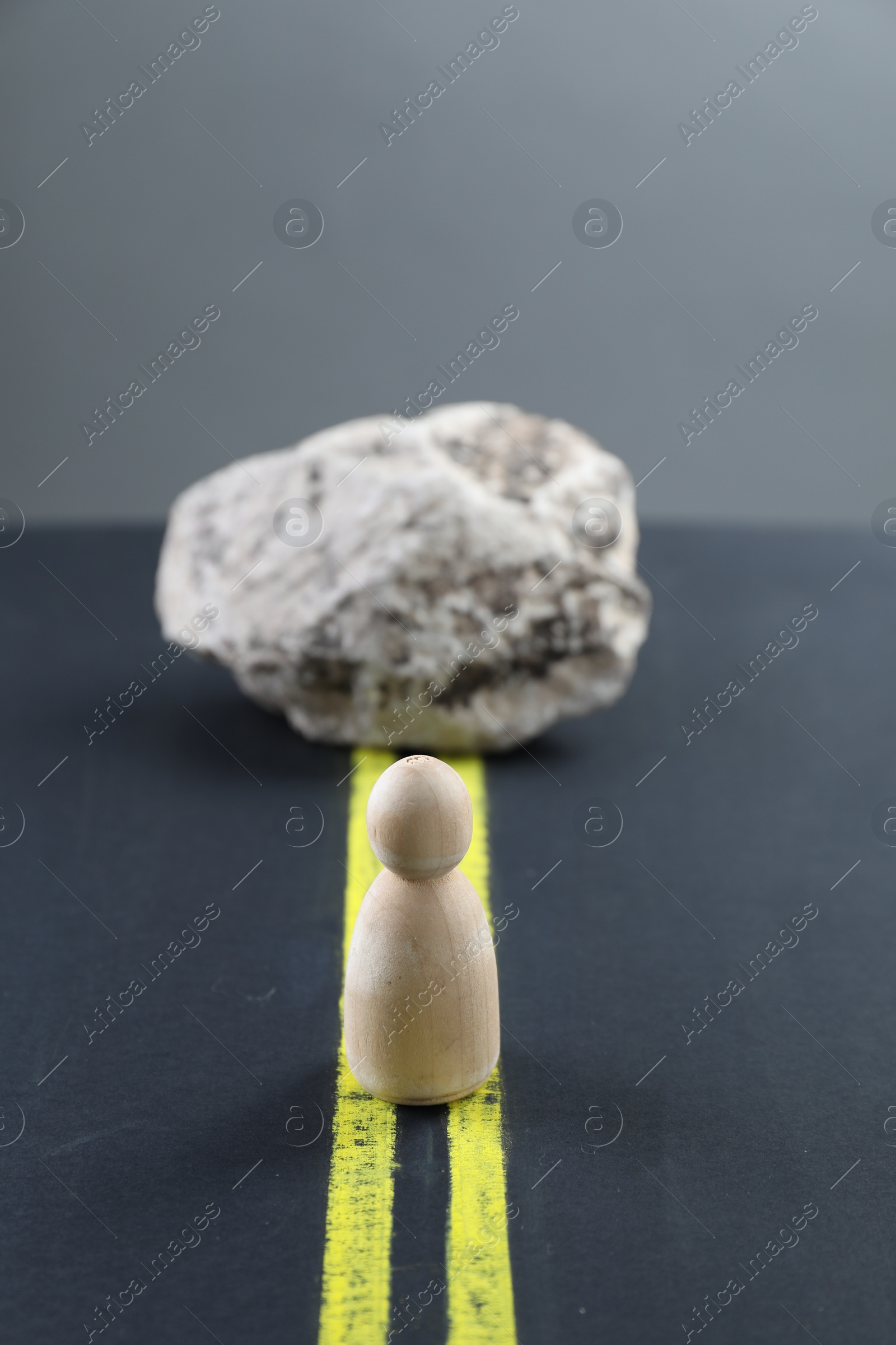 Photo of Overcoming barries for development and success. Wooden human figure in front of stone on road