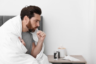 Photo of Sick man coughing on bed at home, space for text. Cold symptoms