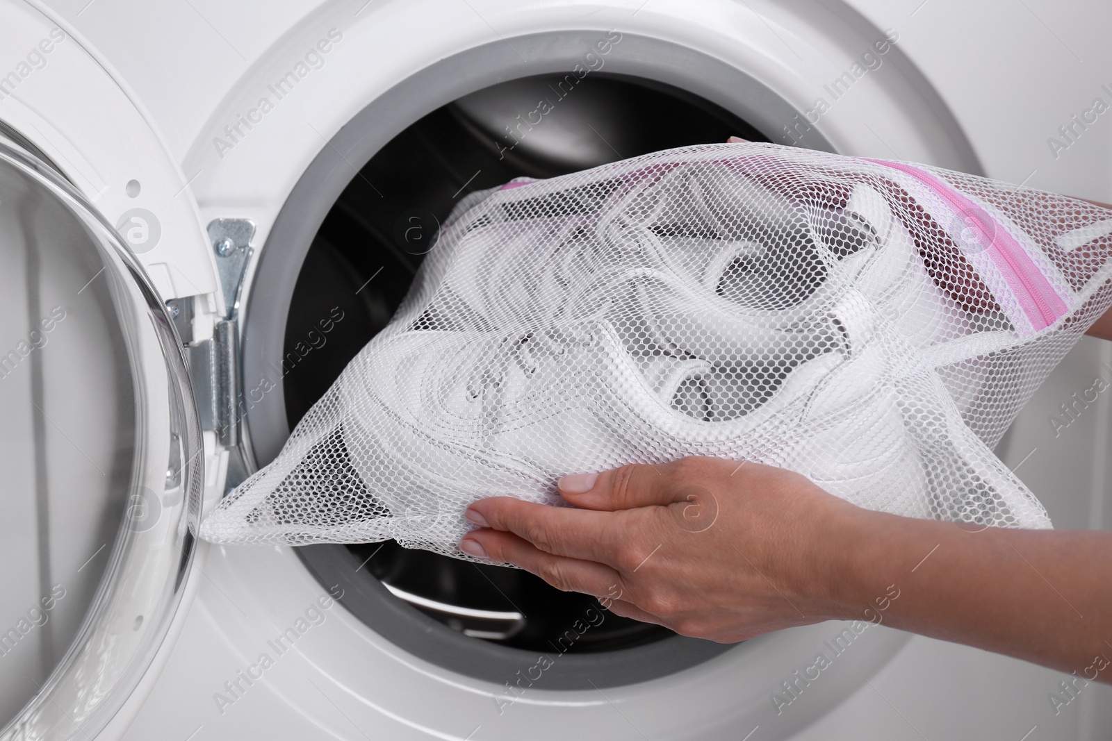 Photo of Woman putting pair of sport shoes in mesh laundry bag into washing machine, closeup