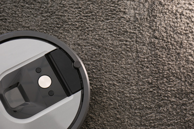 Modern robotic vacuum cleaner on dark carpet, top view. Space for text