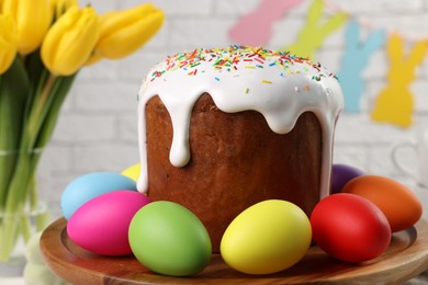 Photo of Tasty Easter cake and decorated eggs on wooden stand, closeup