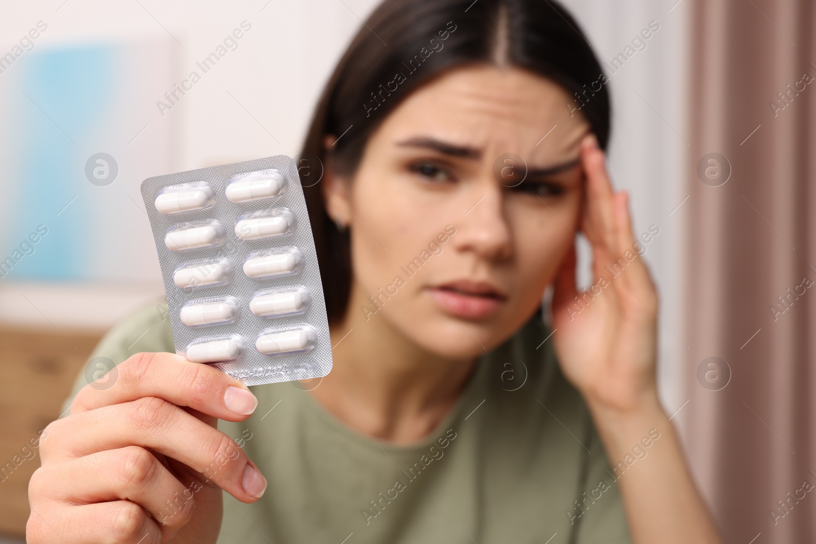 Photo of Sad woman with blister of pills suffering from headache indoors, selective focus