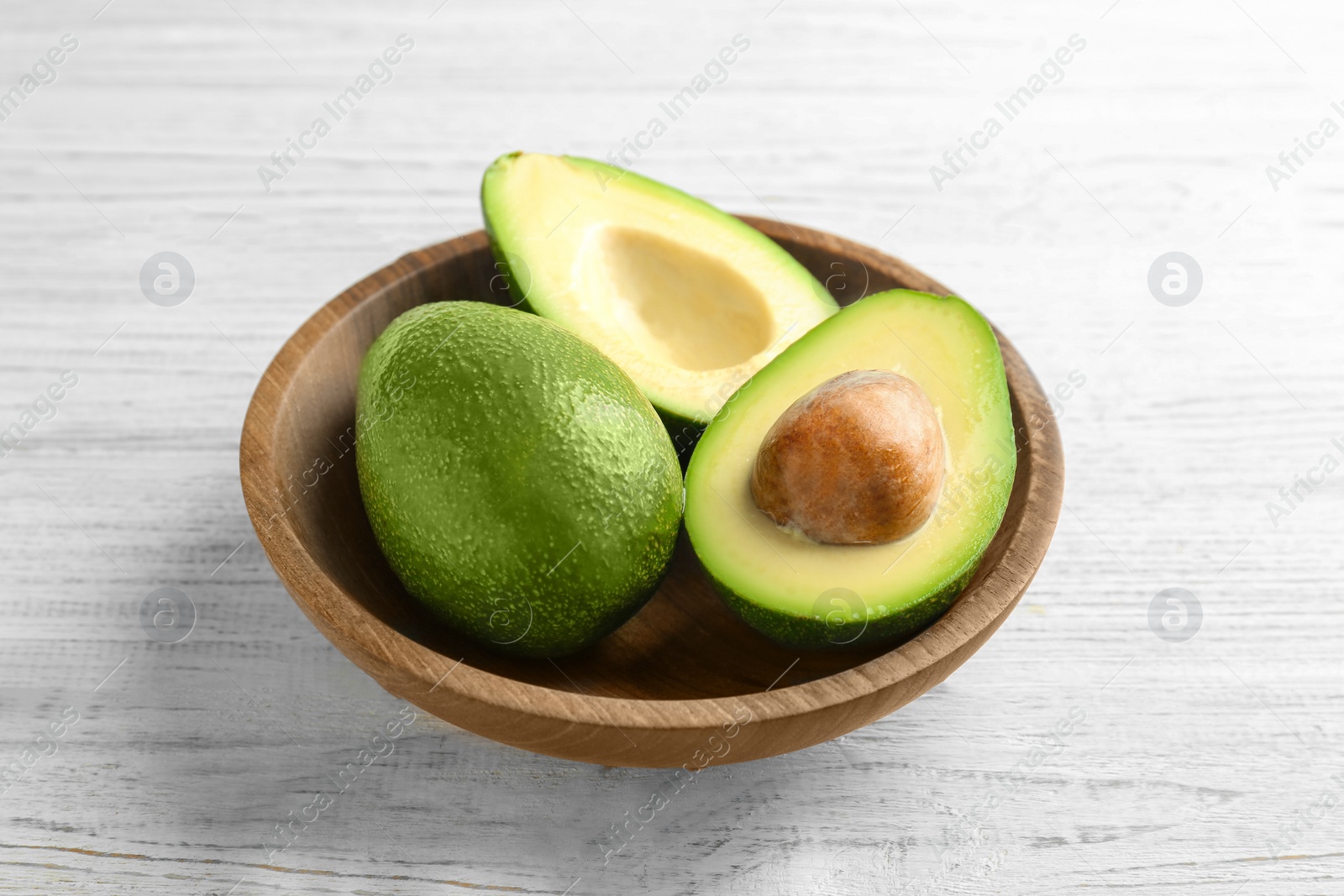 Photo of Bowl with ripe avocados on wooden background