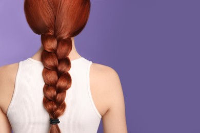 Woman with red dyed braided hair on purple background, back view. Space for text