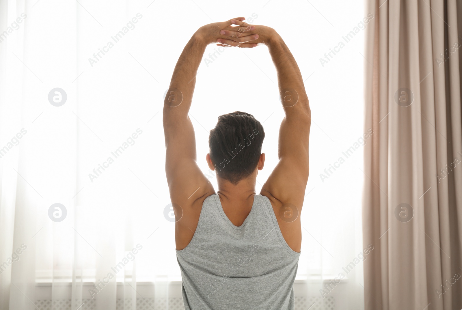 Photo of Man stretching near window at home. Lazy morning