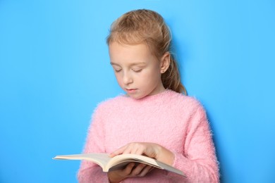 Little girl reading book on light blue background
