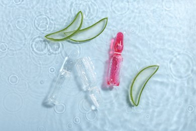 Skincare ampoules with extract of aloe vera and cut leaves in water on light blue background, flat lay