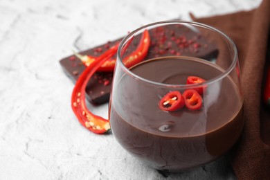 Glass of hot chocolate with chili pepper on white textured table, closeup. Space for text