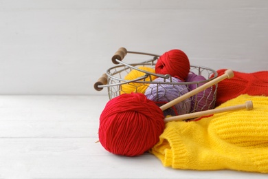 Photo of Soft woolen yarns with knitting needles and sweater on white table, space for text