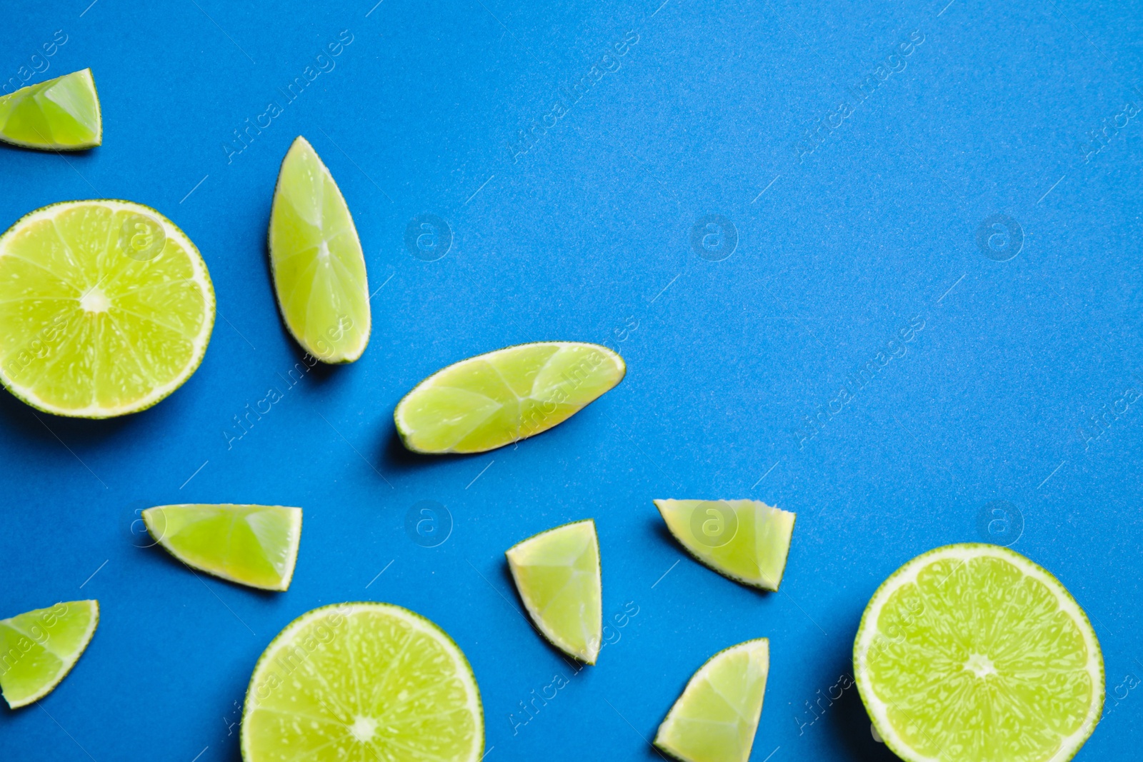 Photo of Juicy fresh lime slices on blue background, flat lay. Space for text