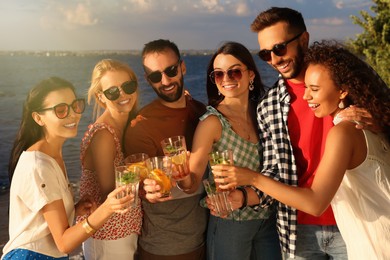 Group of friends with drinks having fun near river at summer party