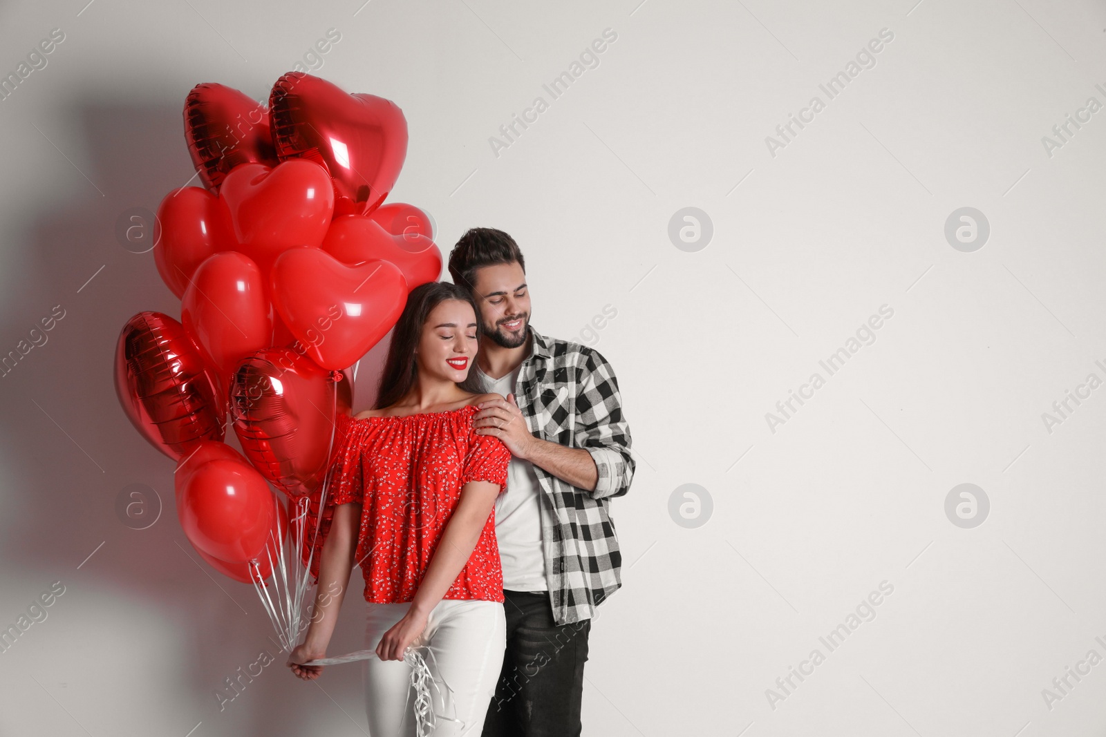 Photo of Happy young couple with heart shaped balloons on light background, space for text. Valentine's day celebration