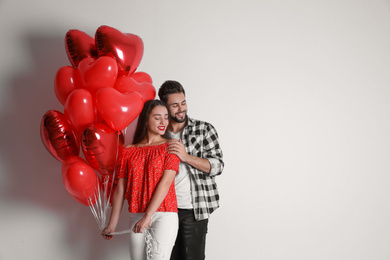 Happy young couple with heart shaped balloons on light background, space for text. Valentine's day celebration