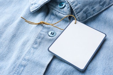 Photo of Blank tag on denim shirt, closeup view. Space for text