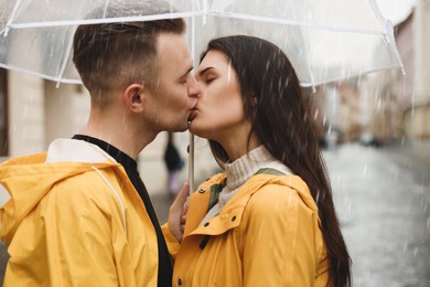 Photo of Lovely young couple with umbrella kissing on city street