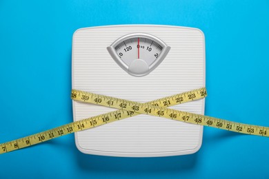 Photo of Bathroom scale tied with measure tape on light blue background, top view