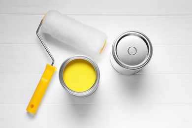 Can of yellow paint, closed one and roller on white wooden table, flat lay