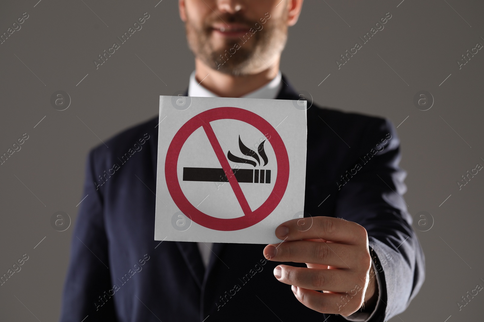 Photo of Man holding card with no smoking sign on gray background, closeup