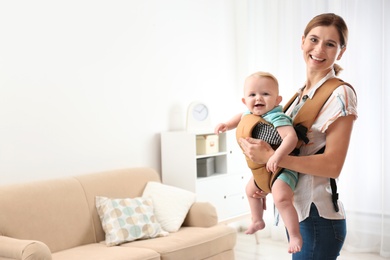 Woman with her son in baby carrier at home. Space for text