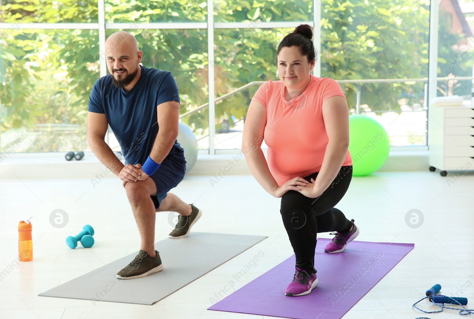 Photo of Overweight man and woman doing exercise on mats in gym