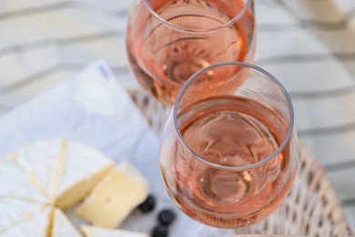 Glasses of delicious rose wine, food and basket on white picnic blanket, closeup