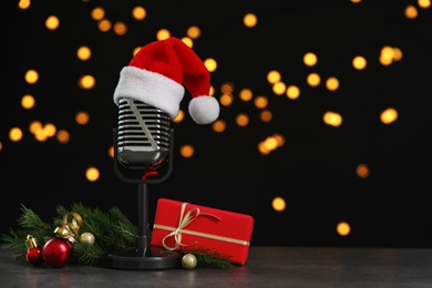 Microphone with Santa hat and decorations on grey table against blurred lights, space for text. Christmas music