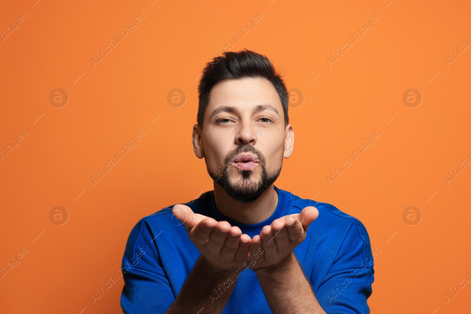 Photo of Handsome man blowing kiss on orange background