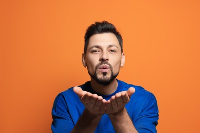 Photo of Handsome man blowing kiss on orange background