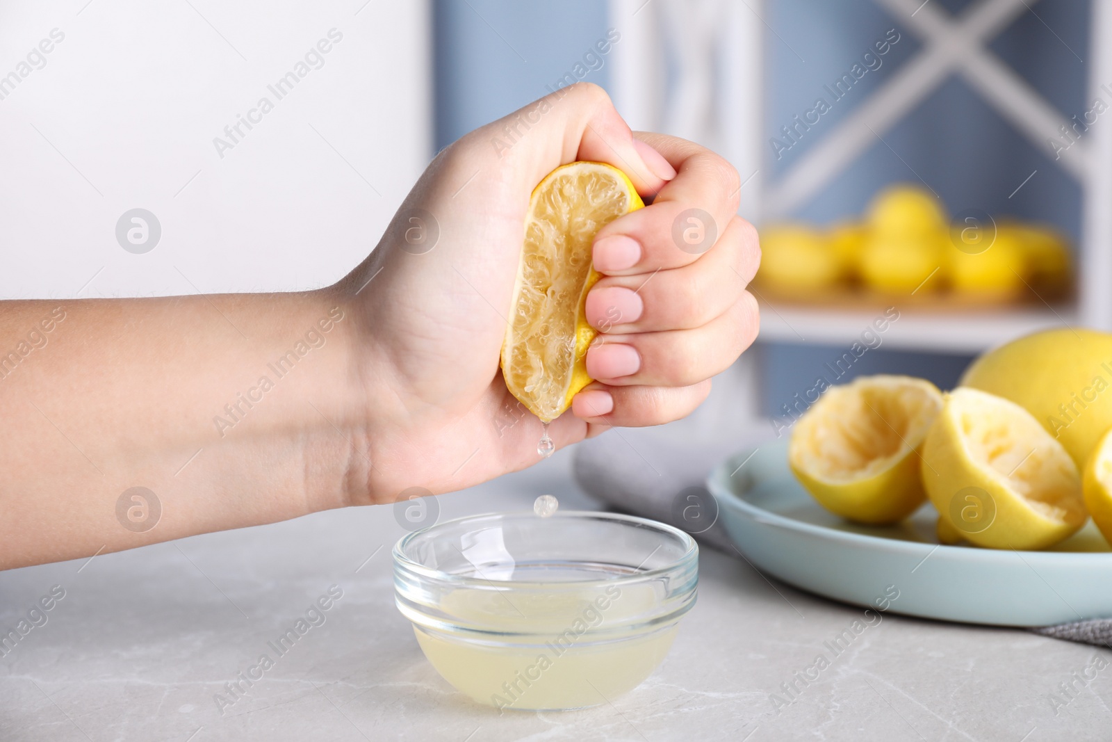 Photo of Woman squeezing lemon juice into glass bowl at grey marble table, closeup